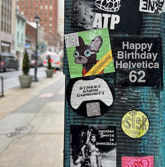 Helvetica font sticker on street pole for its birthday.